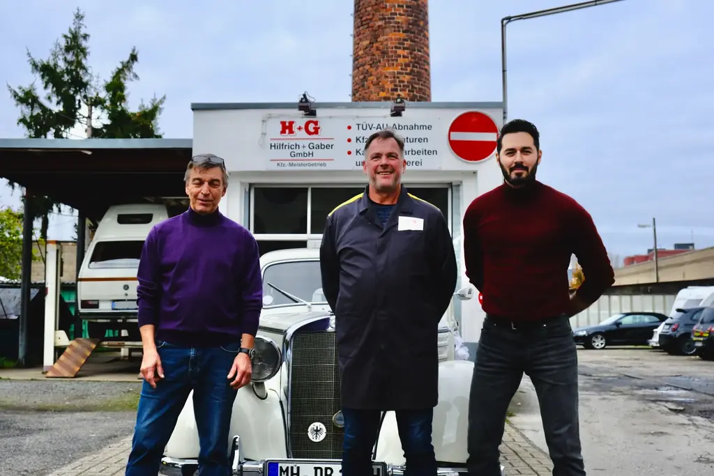 Das Team von Hilfrich + Gaber vor dem Firmenschild mit einem Mercedes-Oldtimer